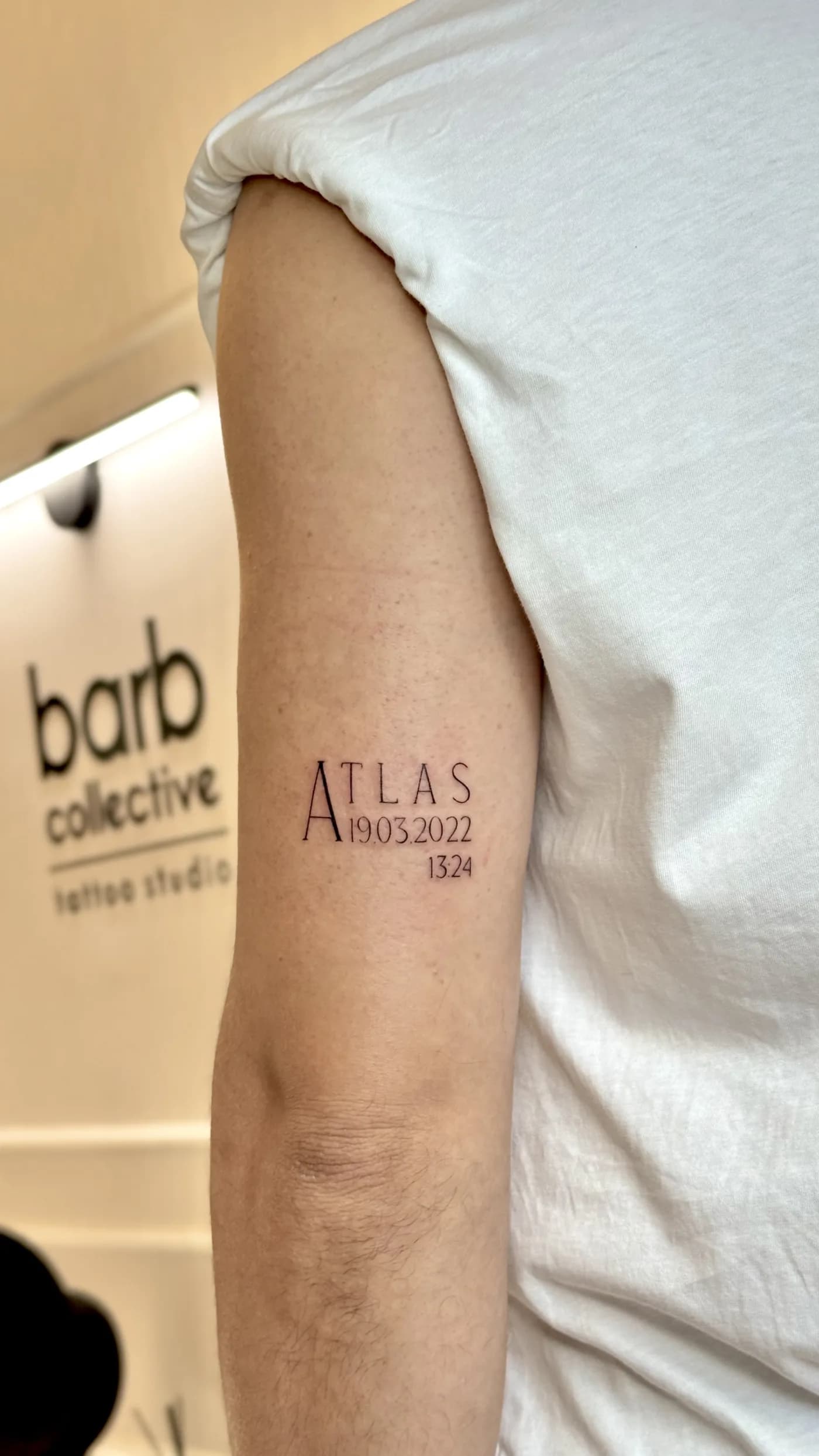 A fine-line lettering tattoo reading Atlas on the upper arm